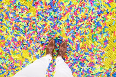 Top down view of legs and feet standing atop confetti sprinkled on yellow ground