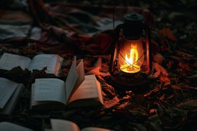 Photo of lit lantern next to 4 to 5 open books on leaves by Tengyart on Unsplash