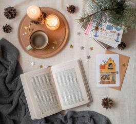 Photo of open book plus book stack, two lit candles, cozy throw, and pinecones by Photo by Olesia 🇺🇦 Buyar on Unsplash